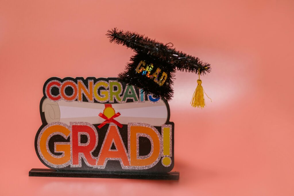 Celebratory 'Congrats Grad' sign with a glittery graduation cap on pink background.